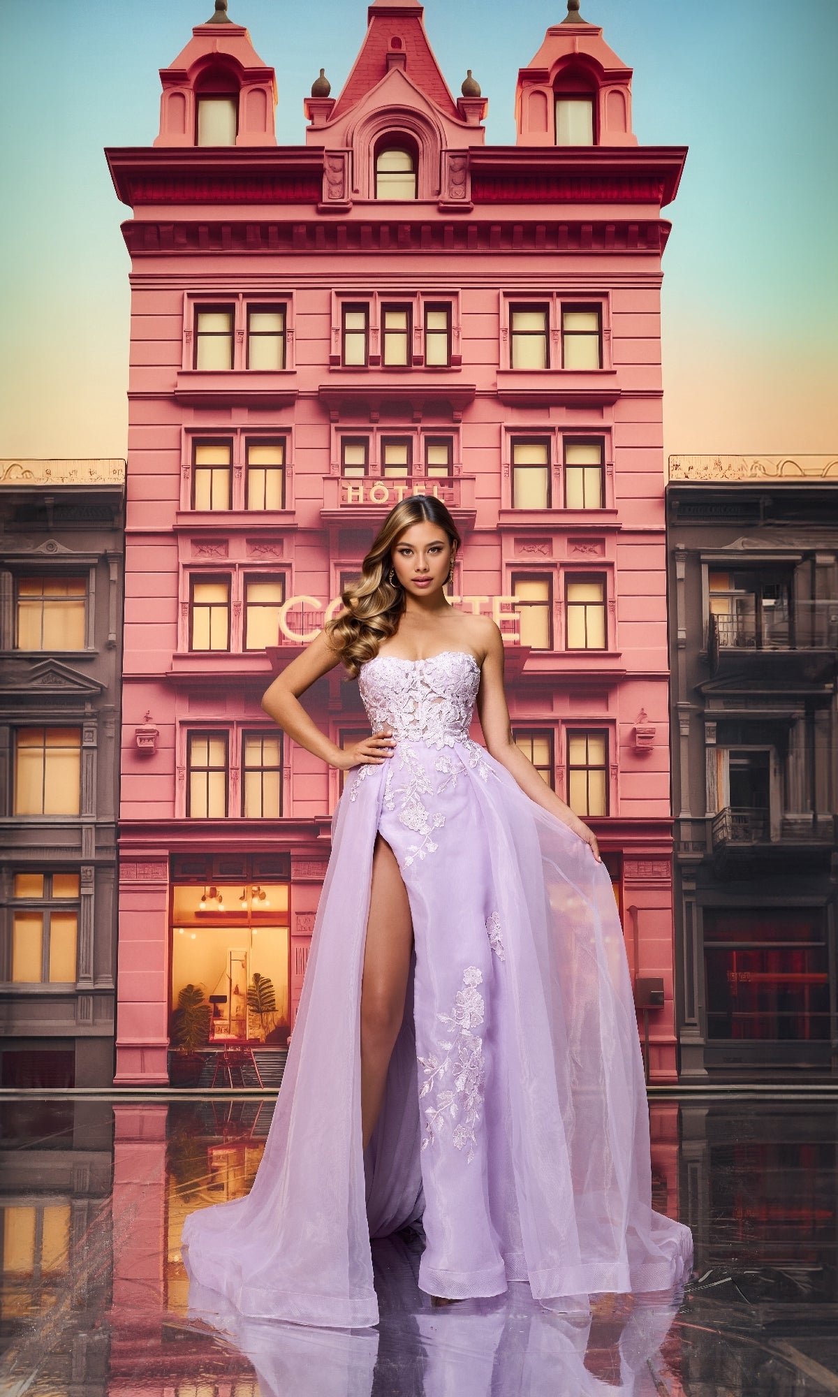 A woman poses confidently in front of a pink hotel wearing the Colette CL8660 Long Prom Dress—a lilac strapless ball gown featuring a sheer lace bodice and high slit.